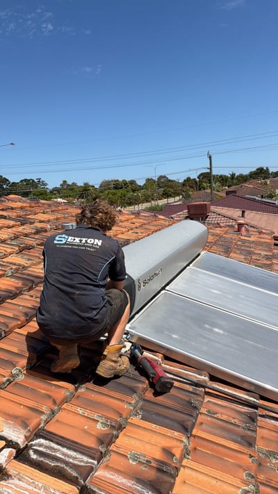 Plumber installing a Rheem hot water system against an external brick wall