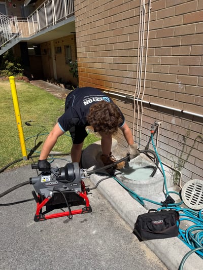 Plumber feeding a CCTV drain camera into an outdoor inspection point